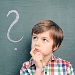 kleiner Junge vor einer Tafel mit Fragezeichen